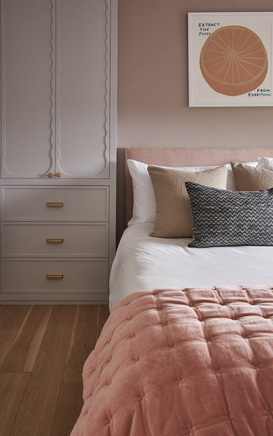 Feminine bedroom with pink bedding, upholstered headboard, and grapefruit artwork